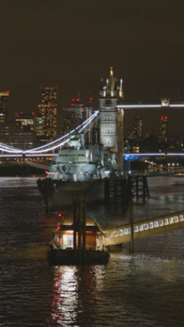 Vertical-Video-Showing-Tower-Bridge-And-City-Skyline-With-HMS-Belfast-On-River-Thames-London-UK-At-Night